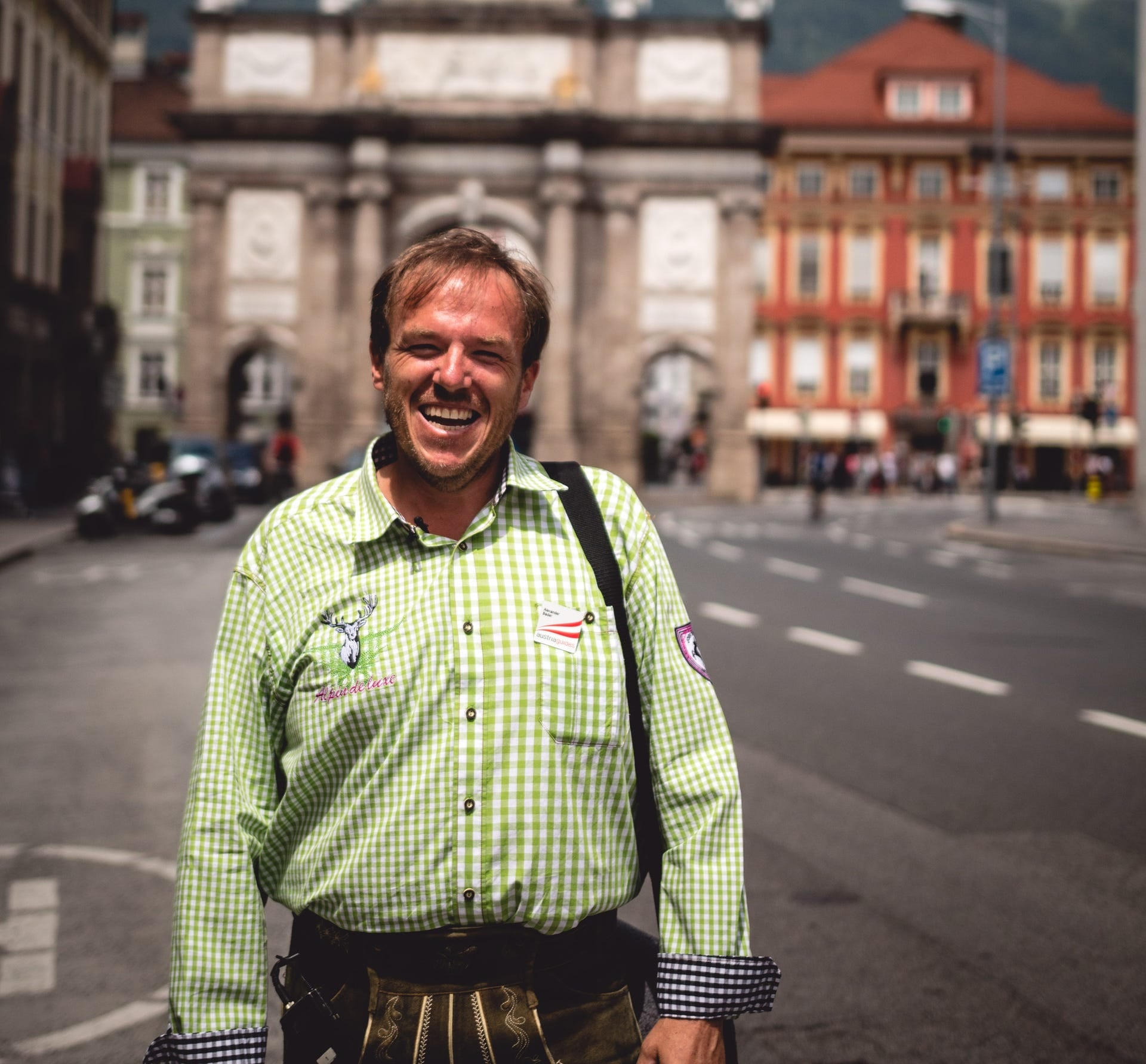 Alexander Bader lacht in Trachtenhemd und Lederhose vor der Triumphpforte in Innsbruck, im Hintergrund die Häuser der Maria-Theresien-Straße.